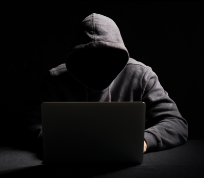 Hooded man with face obscured typing on a laptop
