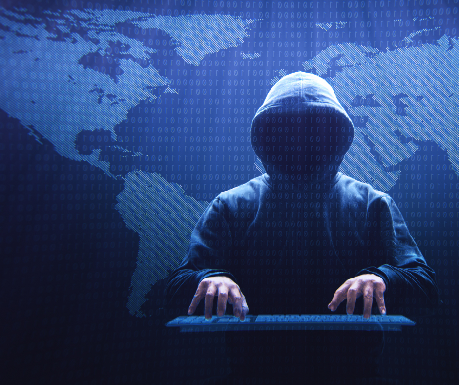 Photo of a hooded figure typing on a keyboard with the map of the world behind them